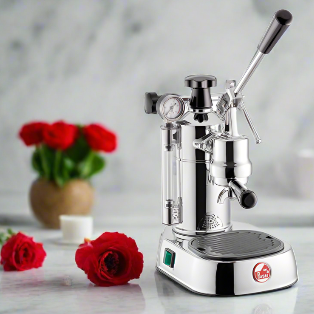 La Pavoni Professional Lusso coffee machine in chrome finish displayed on white counter with red roses in background, featuring manual lever, pressure gauge, and steam wand for authentic Italian espresso brewing